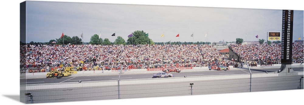 Panoramic photograph taken inside a race track. Cars are shown speeding along with a packed crowd in the stands.