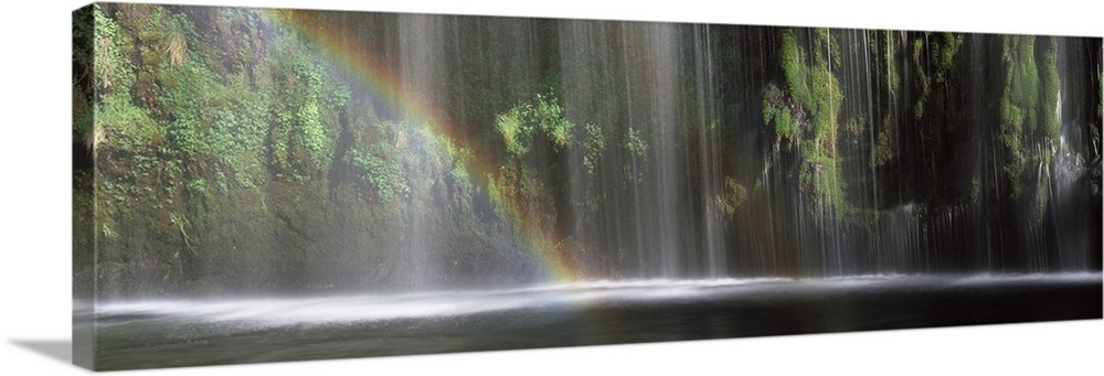 Panoramic photograph of a double rainbow shown in front of a wide waterfall.
