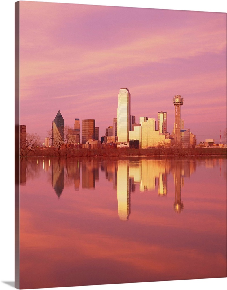 During sunset, the Dallas skyline is photographed from across a body of water that it reflects in.