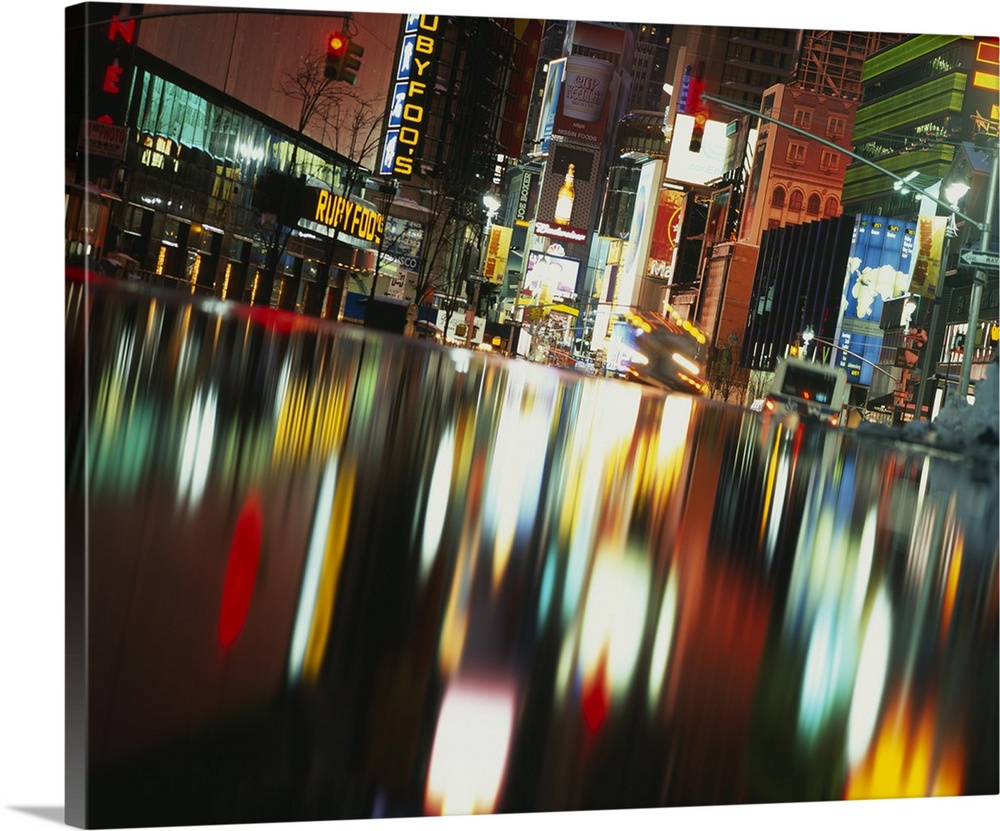 Evening photograph of the city, with neon lights and signs reflected in water, creating an abstract blurred effect.