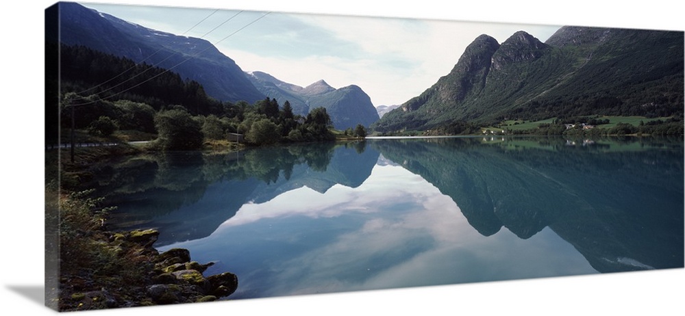 A large piece that is a photograph of mountains lining a body of water that reflect in the still lake.