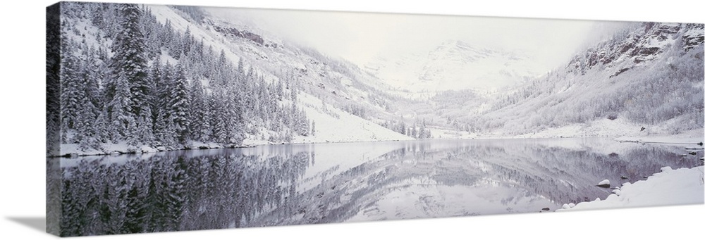Large panoramic photograph of a lake with the reflection of the snow covered trees and mountain in the water.