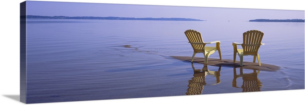 Panoramic photograph of two beach chairs sitting on top of sand bar with land in the far distance.