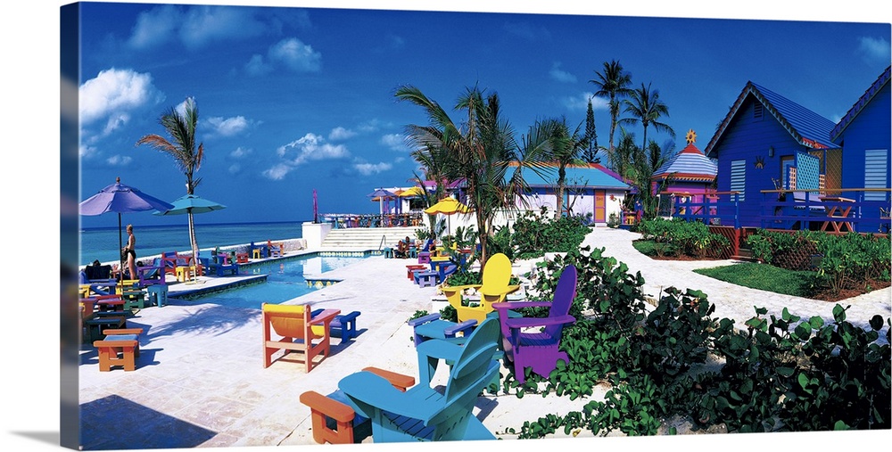 Panoramic photograph of beachfront filled with beach chairs, umbrellas, beach goers, bungalows, and palm trees.
