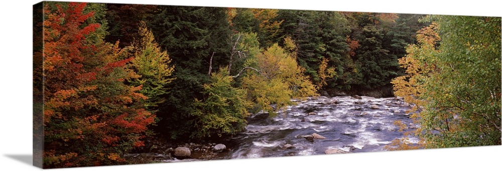 This decorative landscape wall art is a panoramic photograph of a rock filled river riffling through an autumn woodland.