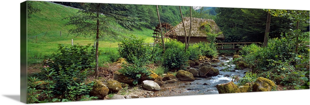 Panoramic wall art of a bucolic scene in this photograph a river filled with moss covered boulders runs through a meadow w...