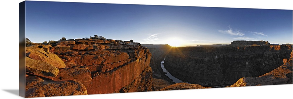 A large panoramic photograph of the Grand Canyon with the river running through it and the sun setting on the horizon.
