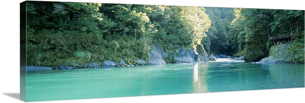 Panoramic image of a river with clear water flowing through a dense forest with big rocks as cliffs on either side.