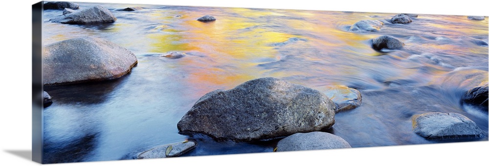Horizontal, big photograph of large rocks in a river, golden autumn colors reflecting in the waters from above.