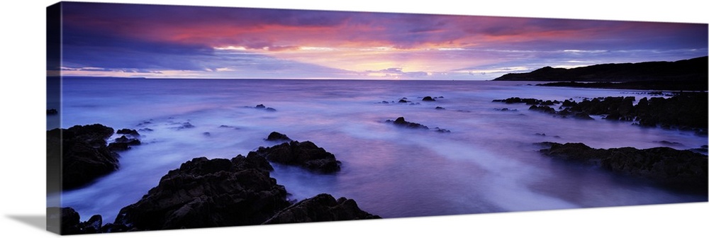 Panoramic photo art of rock formations coming out of the ocean with a sunset in the distance.