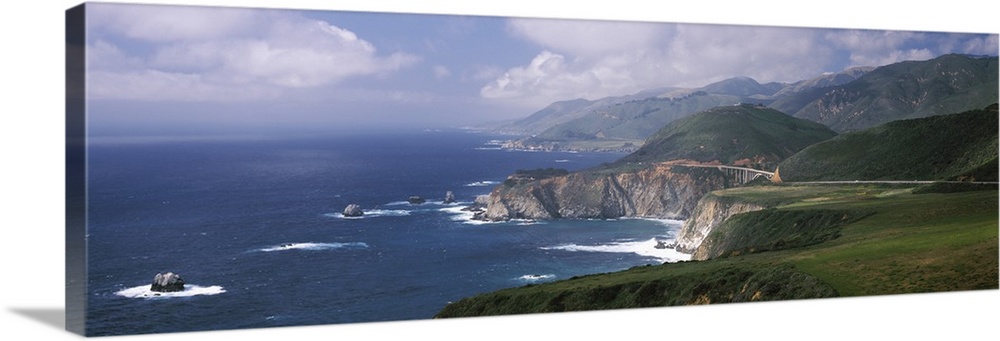 Large panoramic view of rock formations in the pacific ocean and immense mountains along the California coast.