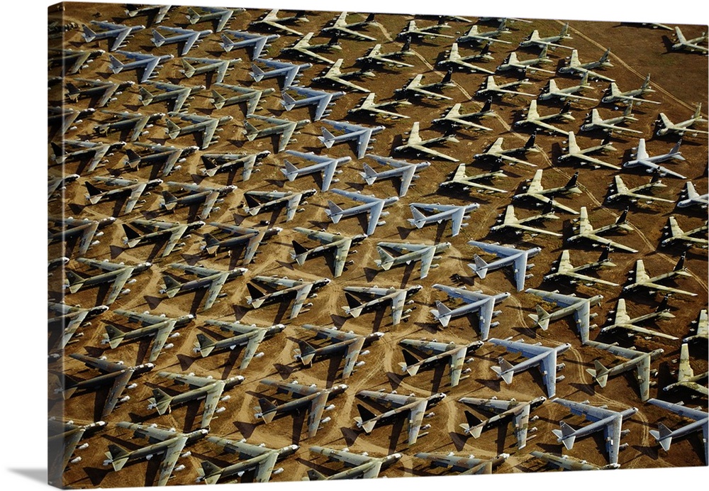 Field of retired airplanes arranged in a geometric pattern in the desert, shining in the sunlight and casting dark shadows.