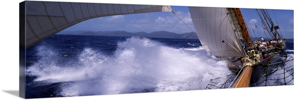 Panoramic photograph of wooden boat with sails making a hard turn and kicking up waves and sea spray in the ocean.