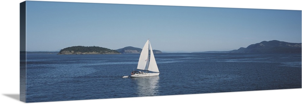 Horizontal and narrow photo on canvas of a sailboat sailing in the ocean with islands covered in forests in the distance.