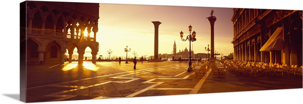 Sun setting on the Piazza di San Marco, its light shining through the historic pillars of the surrounding buildings.