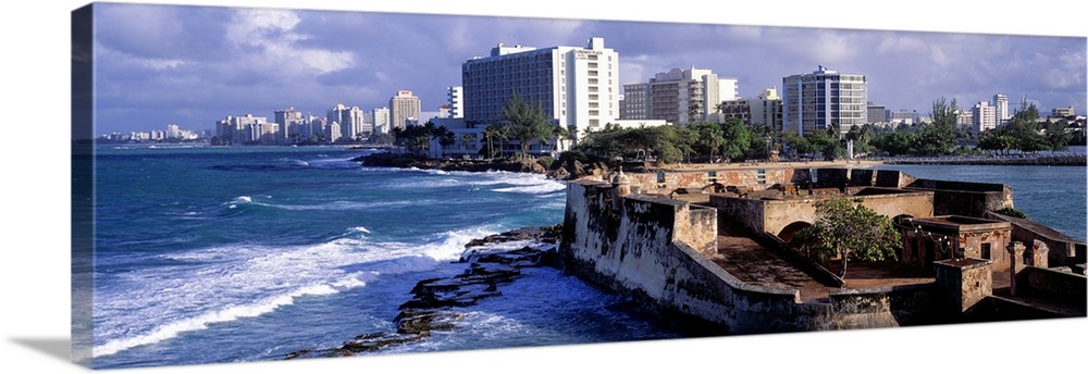 Panoramic photograph of San Jeronimo Fort on the waters of San Juan, the city skyline in the background, in Puerto Rico.
