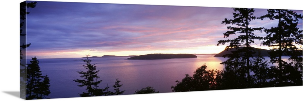 The sunsets below on the ocean in this landscape photograph of small isles off the coast of Washington State in this panor...