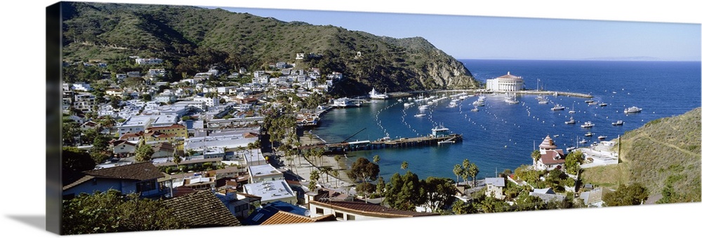 A Pacific coast harbor photographed from a hill side shows numerous docked boats and various buildings in the island village.