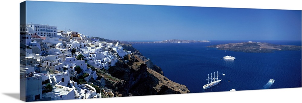 Scenic photo of white houses sitting on the mountain Cliffside in Santorini, Greece with blue ocean water down below.