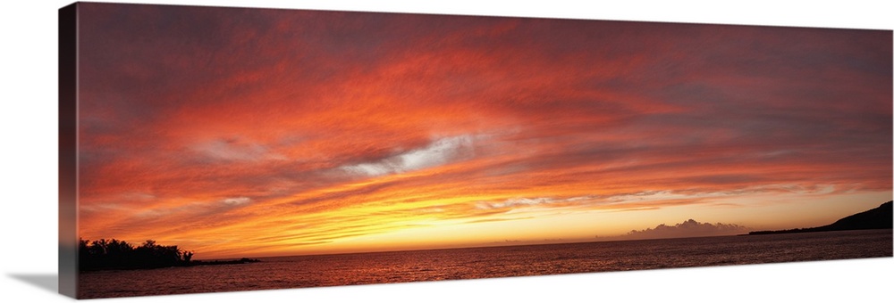 View of the Pacific ocean at sundown. The setting sun creates a glowing light on the clouds above the calm ocean water.