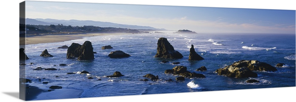 Rock formations in the ocean are pictured in an elongated view as waves form and crash in the water.