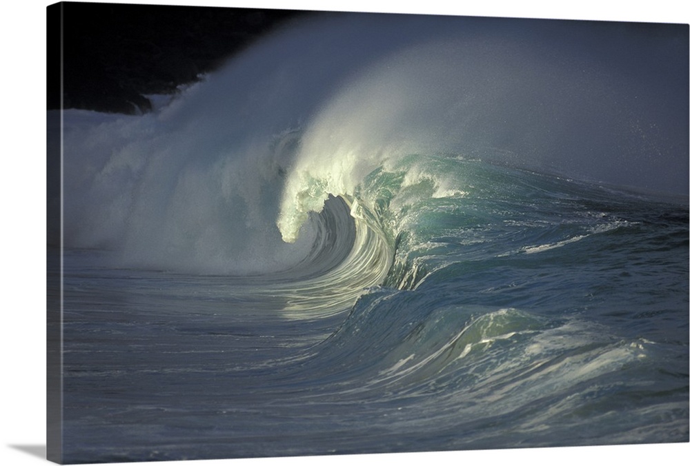 Photograph of a wave curling and crashing as it nears shore with sea mist spraying behind it.