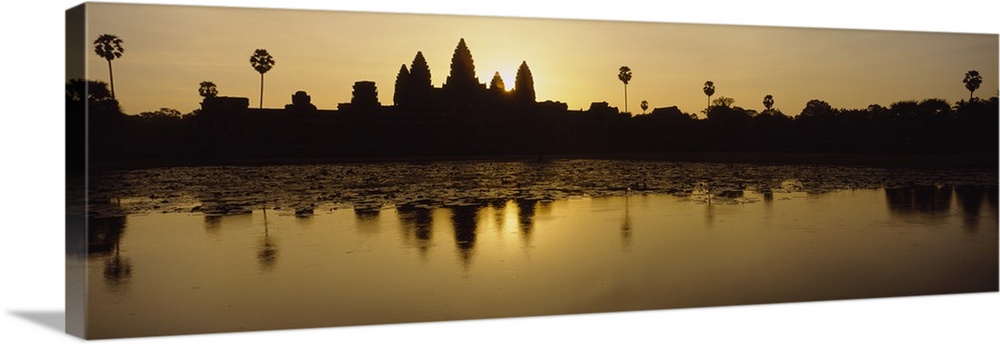 A skyline in Cambodia is pictured from across a body of water and silhouetted by the sunrise just behind it.