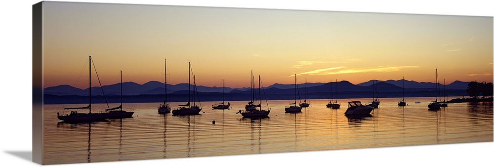 Panoramic photograph of waterway filled with sailboats with mountains in the distance at sunset.  There are ripples in the...