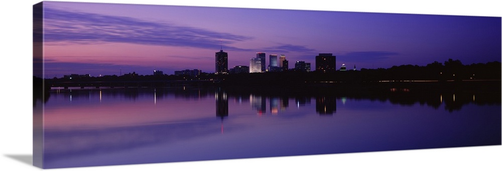 Panoramic photograph taken of buildings sitting on the Arkansas river that are silhouetted by the sunset.