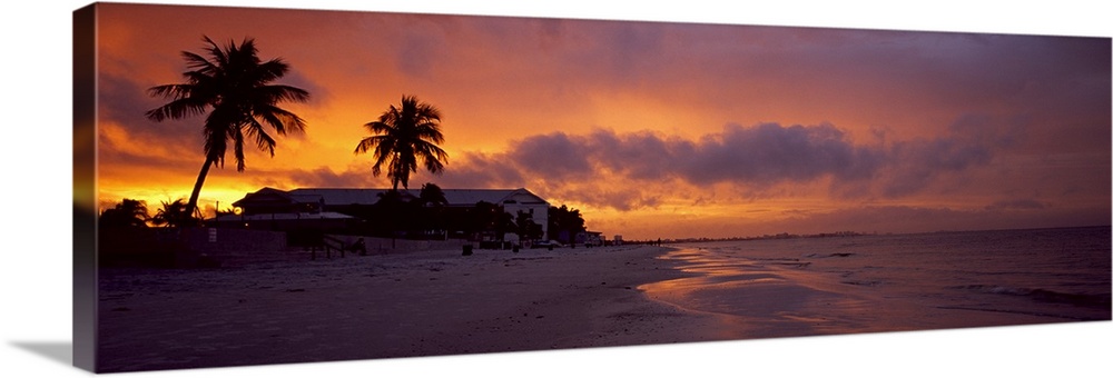 Large panoramic photograph of a coast in Florida with the sun setting that turns the sky various warm colors. Silhouettes ...