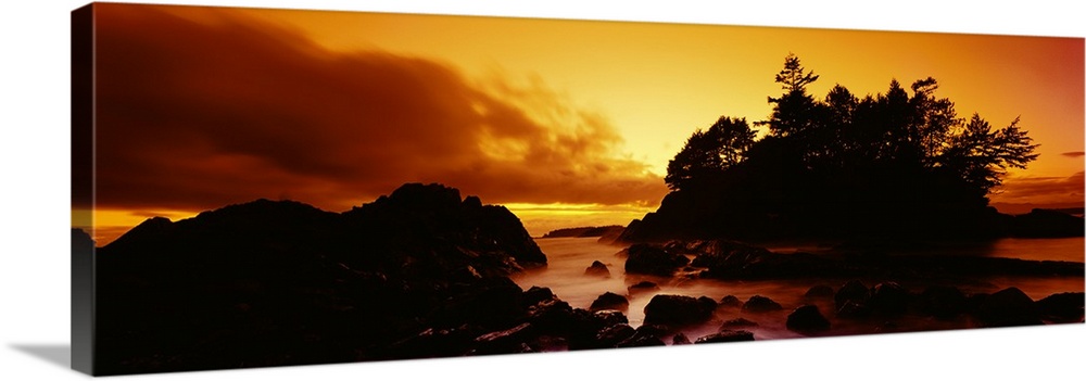 Panoramic photograph displays a sunburnt sky as the sun begins to set over the profile of a rocky shoreline in North America.
