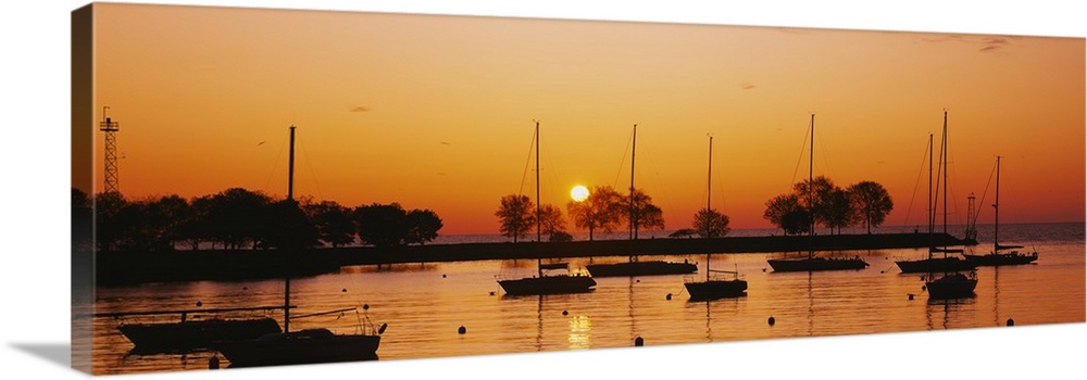 This is a panoramic photograph of boats floating in a harbor as the sunsets reflecting off the water.