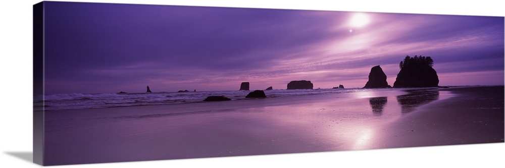 Panoramic photograph taken from a beach with silhouettes of rock formations in the distance as the sun sets and gives the ...