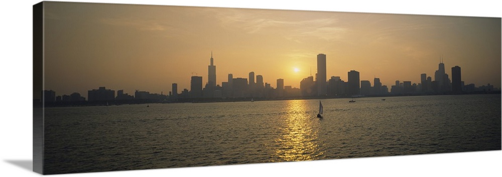 Wide angle photograph of a distant Chicago skyline, silhouetted by the setting sun, several small boats float on the water...