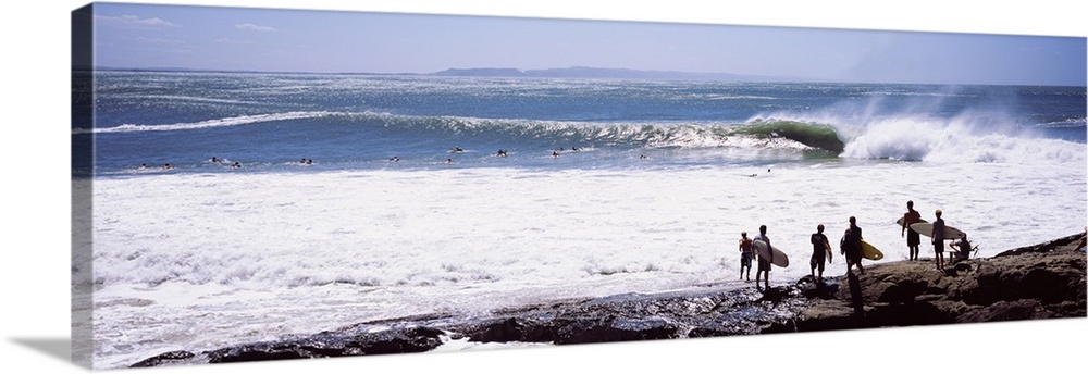 Panoramic photograph of beachgoers at water's edge with waves and ocean in the distance.