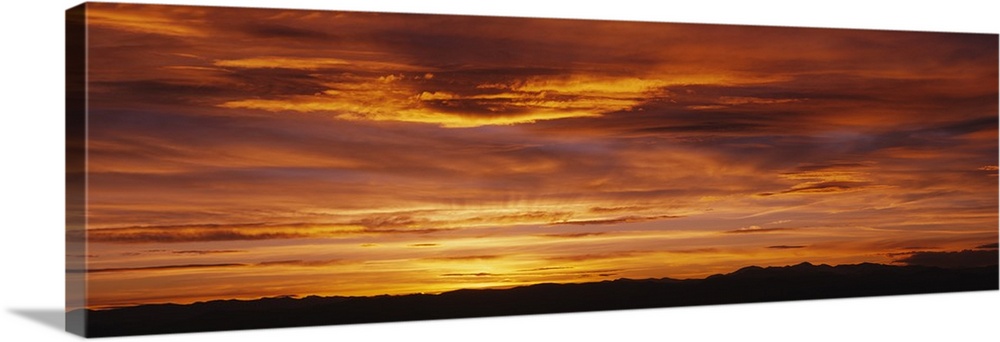 Long panoramic image of the sun setting on the horizon creating a brilliant color show of fire-like colors in the clouds.