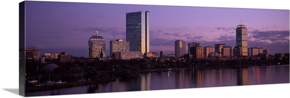 A large panoramic photograph of the Boston skyline showing the river and trees lining the edge in front of the buildings. ...