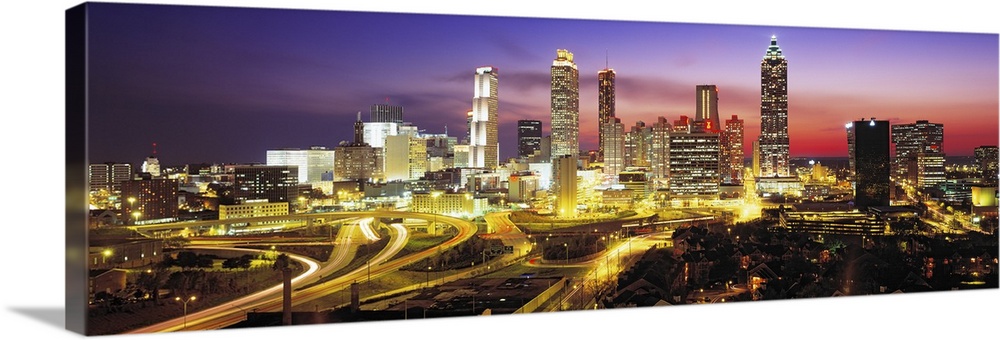 Panoramic photograph of cityscape at night with buildings and streets lit up in the dark colorful sky.