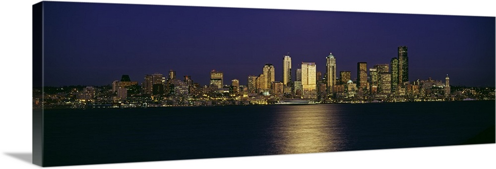 Wide angle, distant photograph of the Seattle skyline, lit at night, over Elliott Bay in Washington.