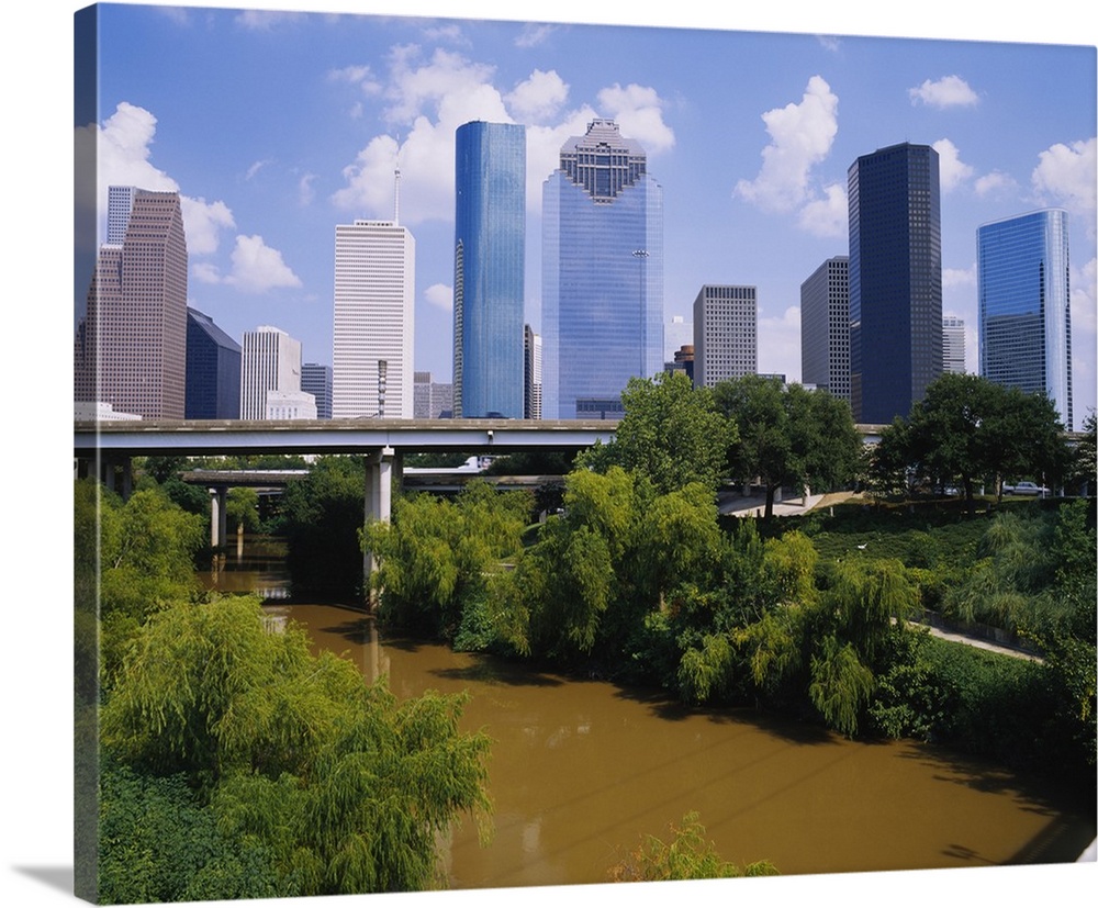 This is a nearly square landscape photograph of cityos downtown skyscrapers and a river that passes through a park and und...