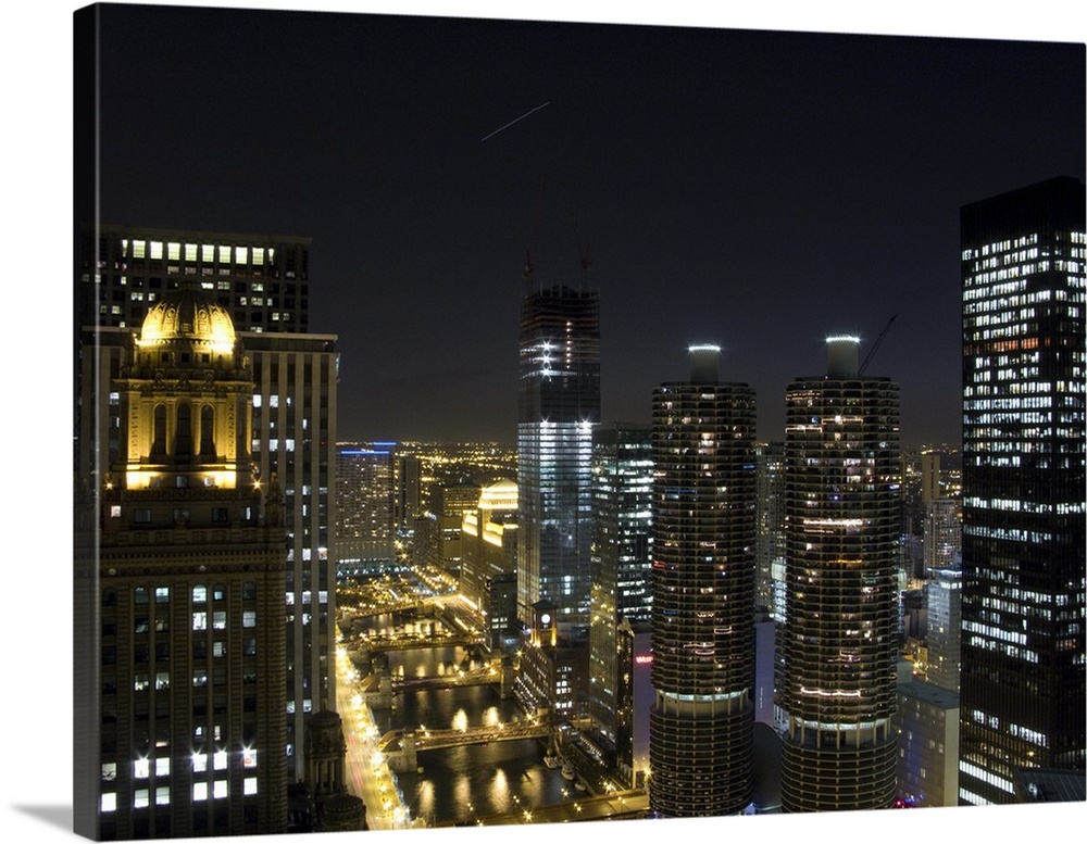 Tall buildings in Chicago are illuminated under a night sky that has a single shooting star photographed.