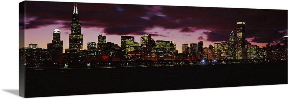 Wide angle photograph of the Chicago, Illinois skyline at night with brightly lit buildings against a deep purple sky.