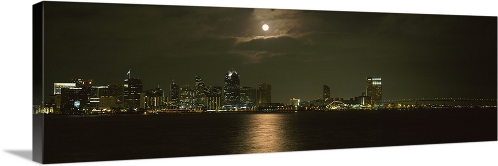 Panoramic photograph taken at nighttime shows a distant view of the brightly lit skyline within a busy city off the coast ...