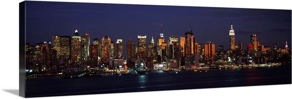 Panoramic photograph of skyscrapers filling the skyline of Manhattan in New York at night.  The bright lights of the build...