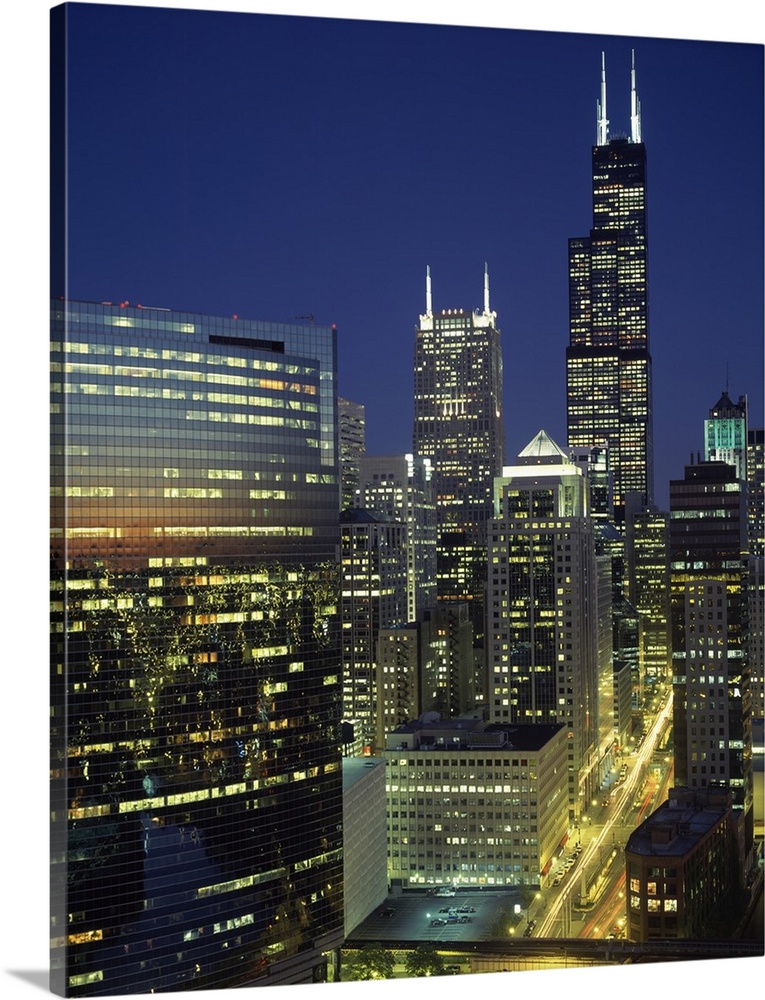 Vertical, high angle photograph overlooking Wacker Drive in Chicago, surrounded by lit buildings at dusk, including the Se...