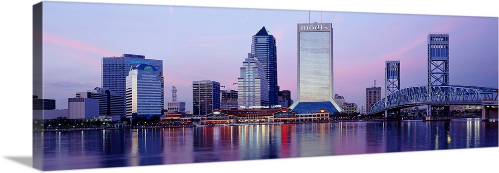 A panorama view of the city skyline in Jacksonville during dusk. The buildings lights reflect in the water that sits in fr...