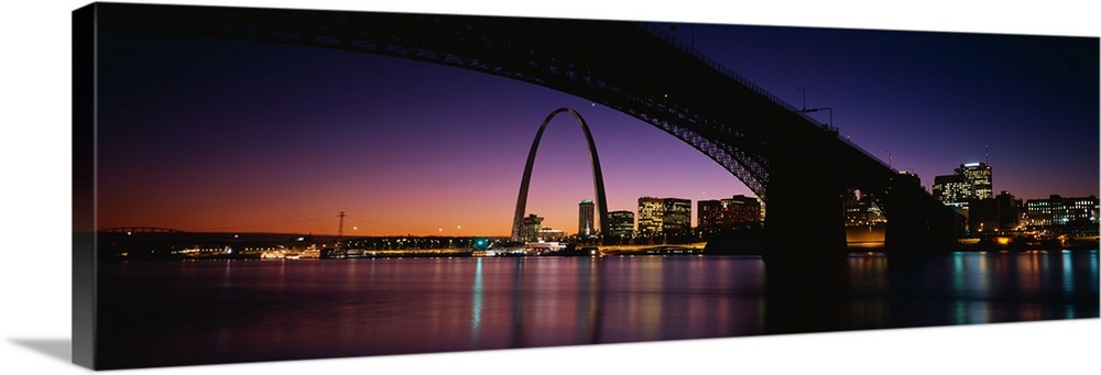 A dramatic panorama of downtown St. Louis including bridges, the arch and sunset.
