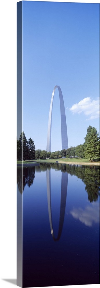 A tall panoramic piece of the famous gateway arch that is photographed from the side over a body of water which it reflect...