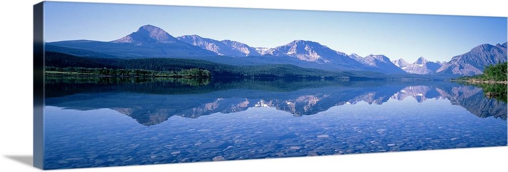 Mountains line the back of this panoramic photograph that is taken from across a crystal clear lake. The land and mountain...