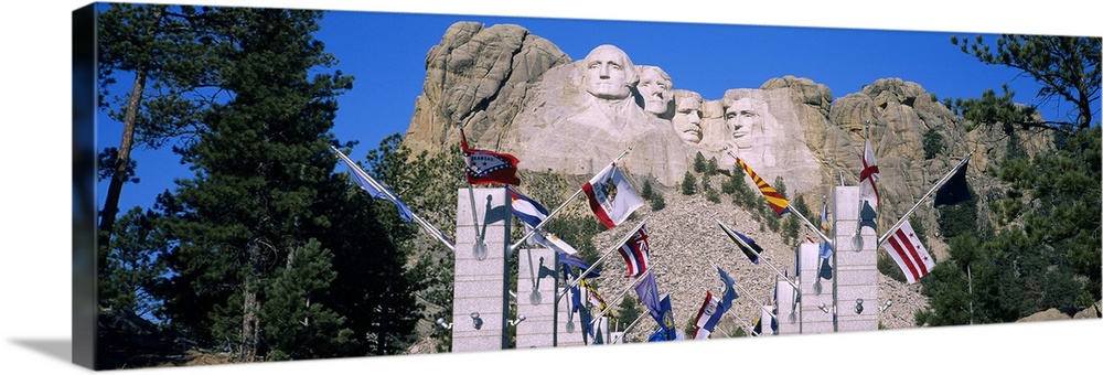 Panoramic photograph of iconic stone memorial carved in mountainside with column and flag lined walkway below.